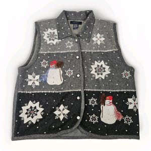 May include: A grey button-up vest with a winter theme. The vest has black accents and embroidered snowflakes and snowmen. The snowmen wear red hats and scarves. White polka dots are scattered across the vest. A festive garment.