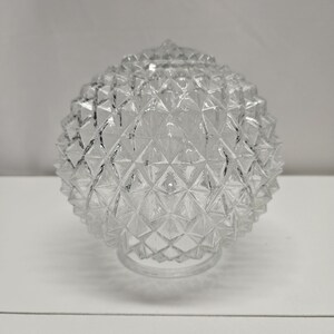 May include: Clear glass globe light fixture with a textured, diamond-shaped pattern. The spherical shade has a rounded top and a circular base. The light fixture is designed to diffuse light and add a decorative element to any room.