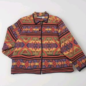 May include: A colorful, patterned jacket with a button-up front. The jacket features a geometric design in shades of red, orange, purple, green, and yellow, with black trim and buttons. The jacket has two front pockets and a collared neckline.