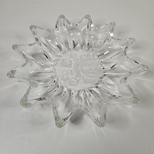 Könnte beinhalten: Klarer, sonnenförmiger Glasteller mit einem mattierten Sonnen- und Monddesign in der Mitte. Der Teller hat spitze Kanten und eine sternförmige Form. Das Glas ist transparent.