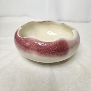 Op de afbeelding: Een kleine, ronde keramische kom met een golvende rand. De buitenkant is diep bordeauxrood van kleur en vervaagt naar wit bij de rand. De binnenkant is crèmewit. De kom is waarschijnlijk voor decoratief of functioneel gebruik.