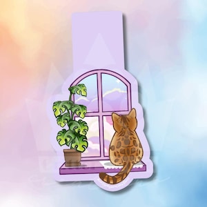 May include: A sticker featuring a cat looking out a window. The cat has brown spots and is sitting on a purple windowsill. A potted plant with green leaves sits next to the window. The window has a purple frame and shows a colorful sky.