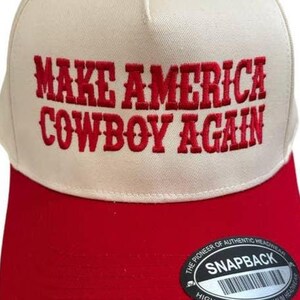 以下が含まれることがあります： 「MAKE AMERICA COWBOY AGAIN」の赤い刺繍が施された白と赤の野球帽。 スナップバック留めとカーブしたつばが付いています。 クラシックなスタイルです。