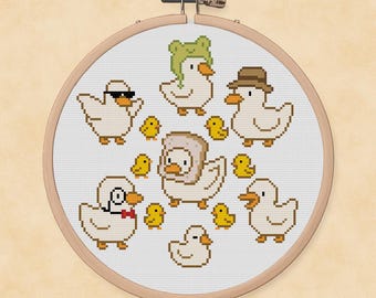Könnte beinhalten: Ein Kreuzstich-Stickrahmen mit einer Ansammlung skurriler Enten und Küken. Die Enten sind mit verschiedenen Accessoires wie Sonnenbrillen und Hüten geschmückt. Die Farbpalette umfasst Weiß-, Gelb- und Brauntöne.