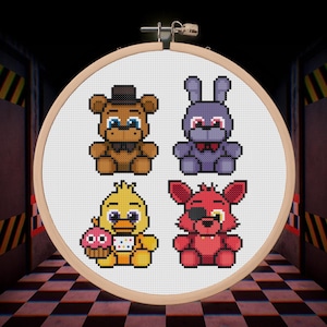 Puede incluir: Un bastidor de punto de cruz con cuatro personajes pixelados: un oso pardo, un conejo morado, un pollito amarillo con una magdalena y un zorro rojo con un parche en el ojo. Fondo blanco.