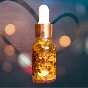 Puede incluir: Una botella de vidrio transparente con una tapa y un gotero de color cobre. La botella est&aacute; llena de un l&iacute;quido amarillo y flores y hierbas secas.