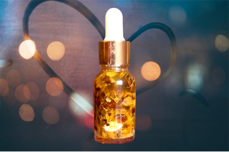 Puede incluir: Una botella de vidrio transparente con una tapa y un gotero de color cobre. La botella est&aacute; llena de un l&iacute;quido amarillo y flores y hierbas secas.
