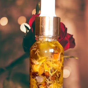 Puede incluir: Una botella de vidrio con tapa dorada y gotero, llena de un l&iacute;quido amarillo y flores secas. La botella est&aacute; enfocada y el fondo est&aacute; desenfocado.