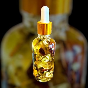 May include: A glass bottle with a gold lid and a white dropper top filled with a yellow liquid and dried herbs and flowers.