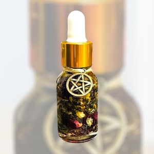 Könnte beinhalten: Kleine Glasflasche mit goldenem Verschluss und weißer Pipette, gefüllt mit dunkler Flüssigkeit und Pflanzenstoffen. Ein silberner Pentagramm-Anhänger hängt am Hals. Die Flasche enthält getrocknete Kräuter und Blütenblätter.