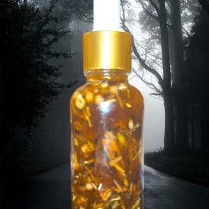 May include: A clear glass bottle with a gold cap and white dropper, filled with a brown liquid containing visible herbs and botanicals. The background features a dark, misty forest scene with a road.