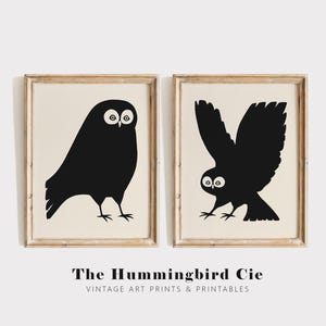 May include: Two framed art prints featuring black owl silhouettes on a cream background. One owl is standing, the other is in flight. The frames are a light wood color. The text at the bottom reads "The Hummingbird Cie" and "Vintage Art Prints & Printables."