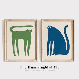 May include: Two framed illustrations of stylized cats. The cat on the left is green and the cat on the right is blue.