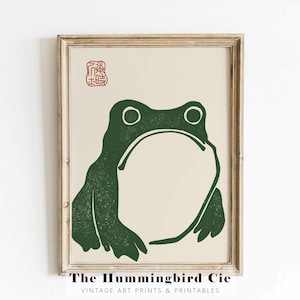 May include: A vintage style print of a green frog with a textured look. The print has a red stamp in the top left corner with Japanese characters. The text below the image reads "The Hummingbird Cie Vintage Art Prints & Printables".