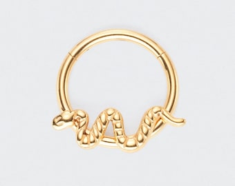 May include: A gold-colored septum ring featuring a detailed snake design. The snake is coiled around the ring, adding a unique and stylish element. The jewelry is designed for nose piercings.