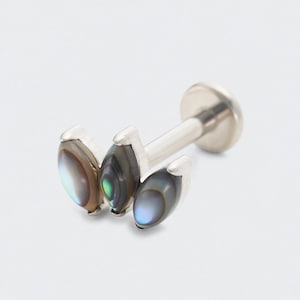 May include: A silver-colored lip piercing with three iridescent abalone shell accents. The abalone shells have a mix of colors, including brown, green, and blue, and are set in a silver bezel.