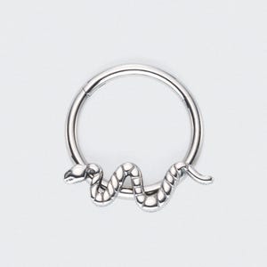 Könnte beinhalten: Ein silberner Septumring mit einem Schlangenmuster. Die Schlange windet sich um den Ring, wobei Kopf und Schwanz nach außen ragen. Der Schmuck besteht aus glänzendem Metall.