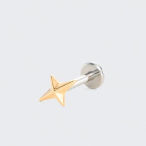 May include: A gold star-shaped labret stud with a silver post and backing. The star has four points and a polished finish. The jewellery is designed for body piercing.