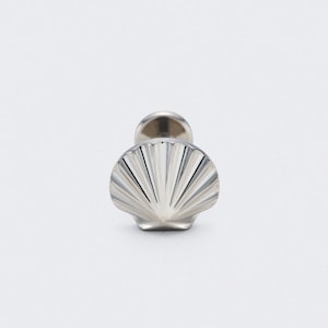 May include: A silver seashell-shaped earring stud. The stud features a detailed, fan-like design and a post for insertion. The earring is set against a white background.