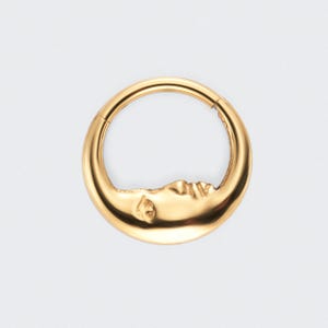 May include: A gold-colored, circular earring with a crescent moon design. The moon's face is detailed with a closed eye and a gentle curve, creating a celestial theme. The earring has a hinged clasp for secure wear.