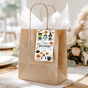 May include: A brown paper gift bag with white tissue paper and a rectangular tag featuring cartoon Halloween characters, pumpkins, bats, and candy. The tag displays the text Happy HALLOWEEN! FROM Anderson in black and orange ink on a white background.