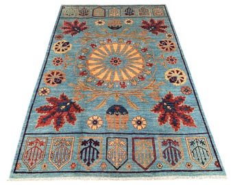 May include: A rectangular, turquoise rug with an intricate floral design. The rug features a central sunburst pattern in yellow and orange, surrounded by stylized leaves and flowers in red, orange, and yellow. The border includes shield-like motifs.