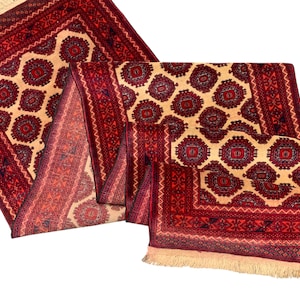 Könnte beinhalten: Aufwendig gemusterter Teppich mit cremefarbenem Feld und dunkelrotem Rand. Der Teppich weist geometrische Muster und Fransen an einer Kante auf. Die Farbpalette umfasst Rot, Creme und Akzente in Marineblau.