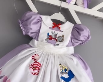 May include: A lavender dress with puff sleeves, a white apron front featuring embroidered characters including a rabbit with a clock, a cat, and a girl, plus card suit appliques. Includes a matching headband with a top hat and white shoes.