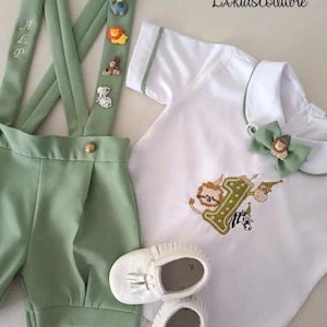 May include: A baby outfit set in white and light green, featuring a short-sleeved shirt with animal embroidery, matching shorts with suspenders, and white leather shoes. The suspenders have decorative animal figures.