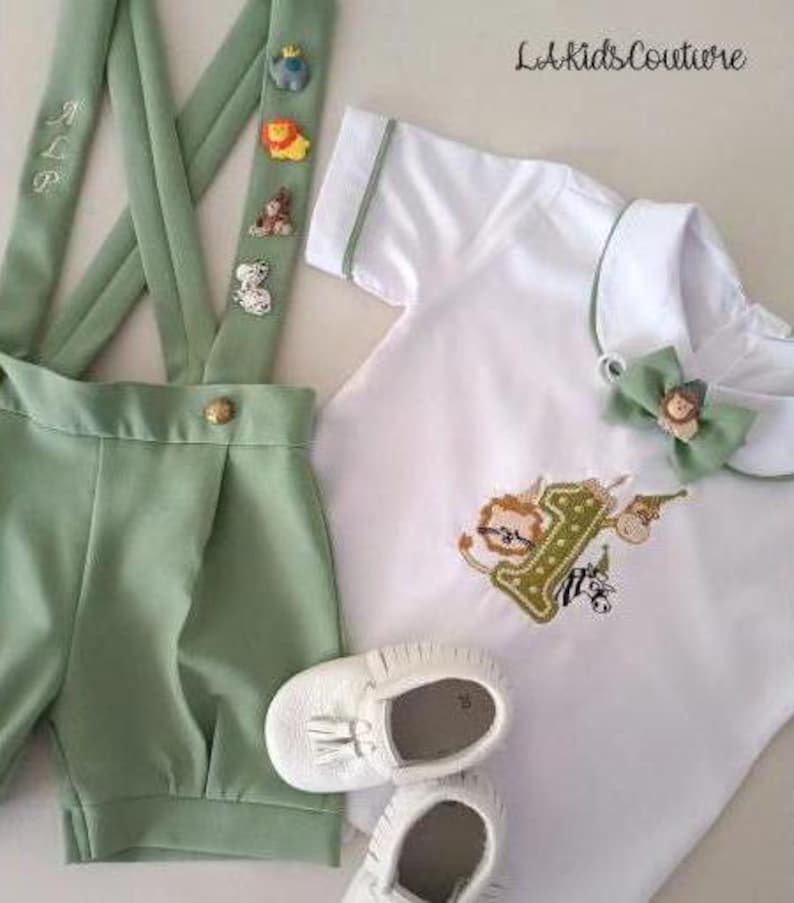May include: A baby outfit set in white and light green, featuring a short-sleeved shirt with animal embroidery, matching shorts with suspenders, and white leather shoes. The suspenders have decorative animal figures.