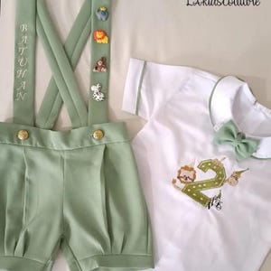 May include: A light green shorts set with suspenders, featuring gold buttons and animal-themed embellishments. The suspenders are embroidered with the name "BATUHAN". A white shirt with green trim and a bow tie, with a number "2" and lion embroidery.