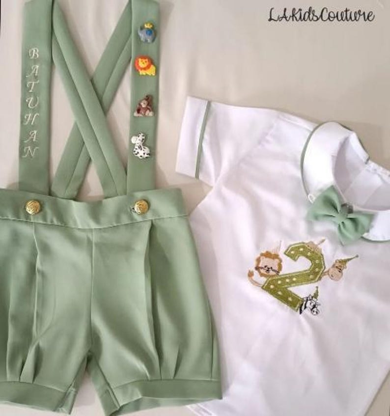 May include: A light green shorts set with suspenders, featuring gold buttons and animal-themed embellishments. The suspenders are embroidered with the name "BATUHAN". A white shirt with green trim and a bow tie, with a number "2" and lion embroidery.