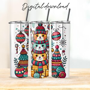 May include: Three stacked cartoon cats wearing Christmas hats and scarves, with ornaments and a Christmas tree on a white tumbler.