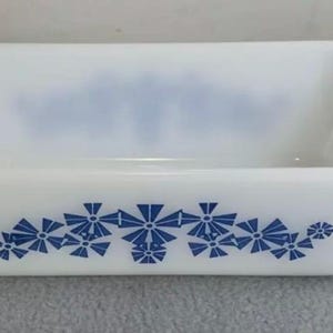 May include: White ceramic loaf pan with a blue floral design. The pan has a rectangular shape and a slightly rounded bottom.