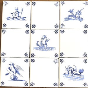 May include: A set of nine square ceramic tiles arranged in a grid, featuring a white background with blue hand-painted illustrations. The designs include mythical creatures like a merman, a unicorn, and a bird, each framed by small blue corner motifs.