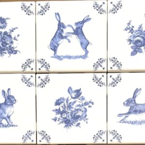 May include: Six white ceramic tiles with blue floral and rabbit designs. The tiles feature various images, including rabbits and flower bouquets. Each tile has a decorative corner pattern.