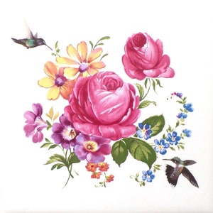 May include: A floral design featuring a cluster of pink roses, yellow daisies, purple pansies, and small orange flowers. Two hummingbirds are depicted in flight near the flowers. The image has a white background.