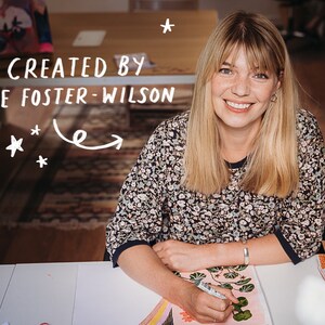 May include: A smiling person with blonde hair and a floral print top is seated at a table. The text "CREATED BY LEE FOSTER-WILSON" is above the person. The person is holding a pen and drawing on a piece of paper. White stars are scattered around the text.