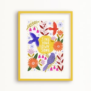 Könnte beinhalten: Ein gelber gerahmter Druck mit weißem Hintergrund, der ein farbenfrohes Blumenmuster mit zwei Vögeln und dem Text "SING YOUR OWN SONG" zeigt.