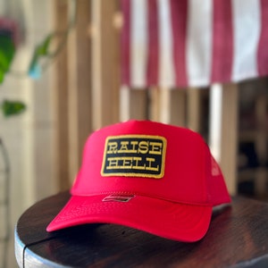 May include: Red trucker hat with a black and gold patch that says "RAISE HELL".