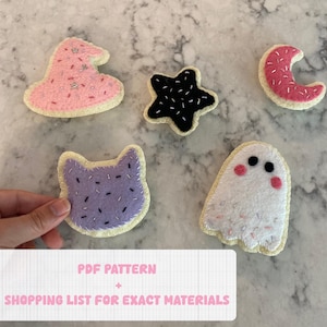 May include: Five felt Halloween cookie ornaments. The cookies are shaped like a witch's hat, a star, a crescent moon, a cat, and a ghost. Each cookie has a different colored frosting and sprinkles.