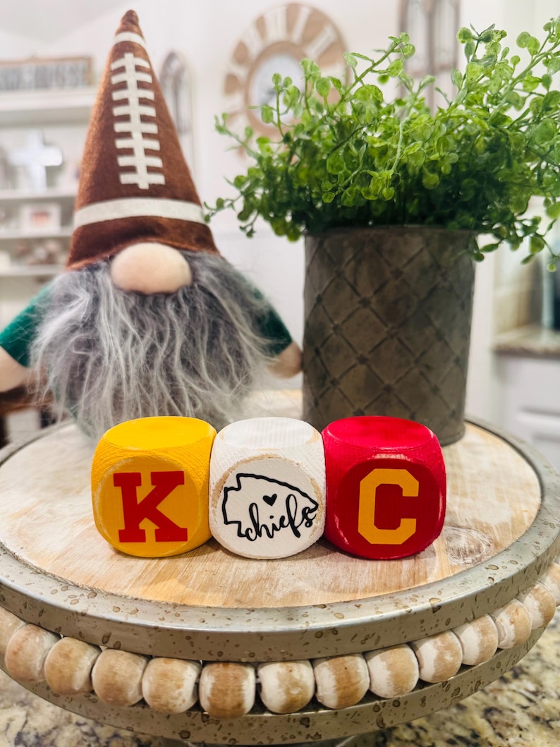 May include: Three wooden blocks with the letters K, C, and a heart with the word "chiefs" inside. The blocks are painted yellow, white, and red with the letters in red.