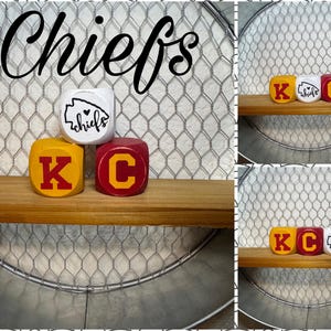May include: Three wooden blocks with the letters "K", "C", and a Kansas City Chiefs logo with the word "chiefs" on it. The blocks are painted in red, yellow, and white.