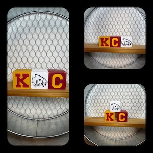 May include: Three wooden blocks spelling "KC Chiefs" with a red and yellow color scheme. The blocks are sitting on a shelf made of wood.