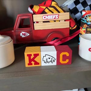 May include: Three wooden blocks spelling out "K.C." in red, yellow, and white with a red heart and the word "chiefs" on the middle block.
