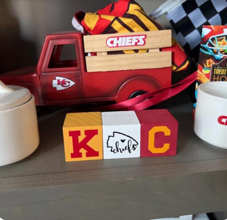 May include: Three wooden blocks spelling out "K.C." in red, yellow, and white with a red heart and the word "chiefs" on the middle block.