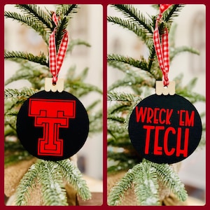 May include: Two black and red Christmas ornaments. One ornament features the Texas Tech University logo, a red "T" with a red circle around it. The other ornament says "Wreck 'Em Tech" in red letters.