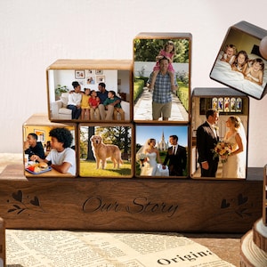 May include: A wooden photo block set displaying family photographs, arranged in a stepped design. The base block is engraved with "Our Story". The photos show family moments, including a wedding, children, and a dog.
