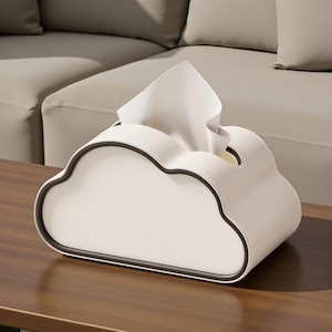 May include: A white cloud-shaped tissue box with a black trim. The tissue box is made of a smooth material and has a slot for dispensing tissues. The design is modern and minimalist, suitable for home decor.