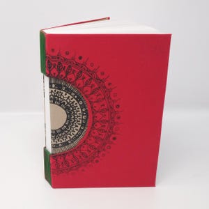 May include: A red journal with a black and white mandala design on the front cover. The journal has a green spine.
